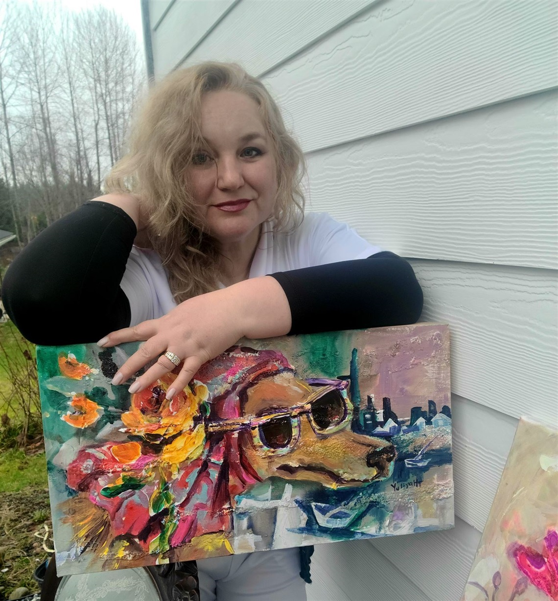 Image of artist Yuliya Helgesen-Thompson holding a piece of her artwork