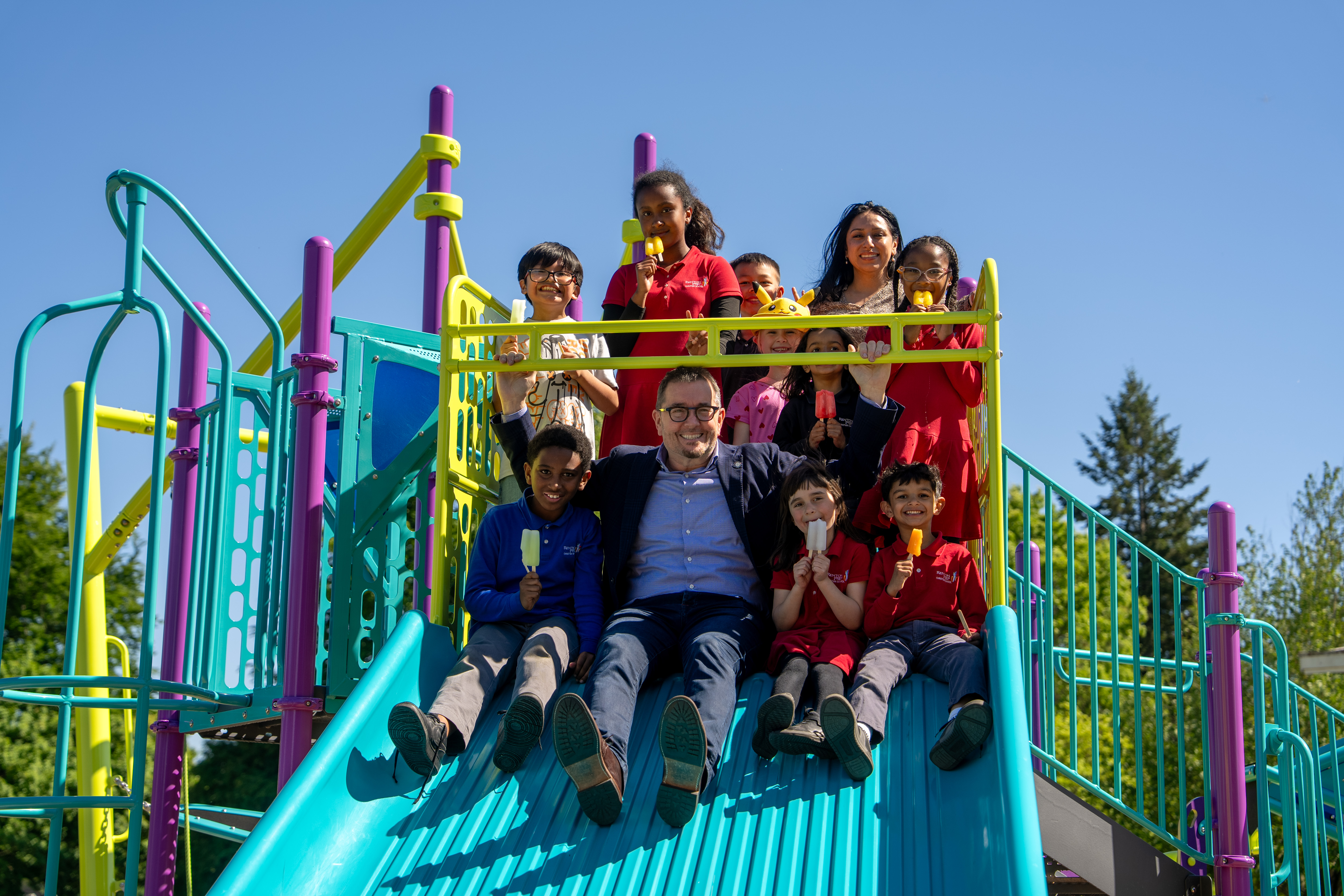 Mayor-Armondo-Pavone-and-Parks-Administratior-Maryjane-Van-Cleave-on-the-playground-slide-with-several-children.jpg