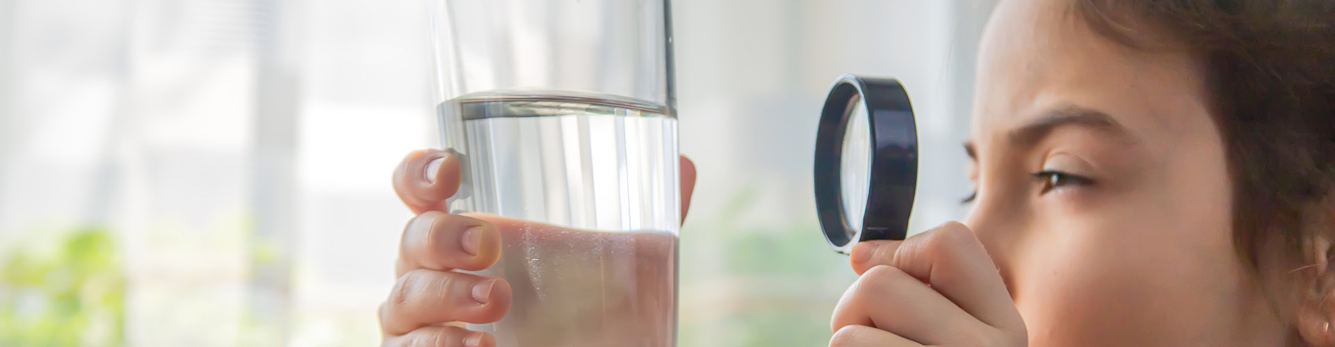 Child looking through magnifying glass at glass of water