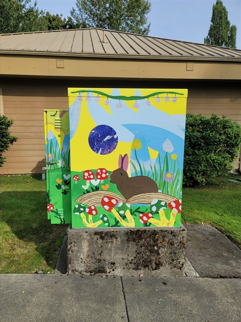 A utility box wrap showing a rabbit in a sunny spring scene with mushrooms and lush green plants.