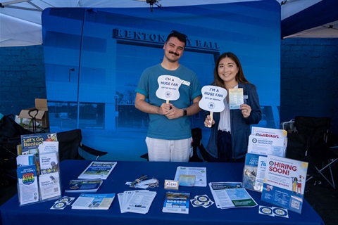 Mini City Hall booth providing city materials and resources with two people holding up fans that say I am a huge fan of Renton