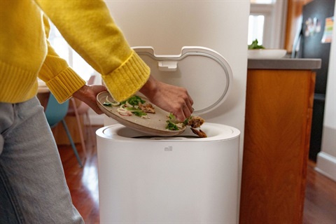 hands scrapping food scraps into a food grounder machine